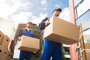 Close up Of Two Delivery Men Carrying Cardboard Box